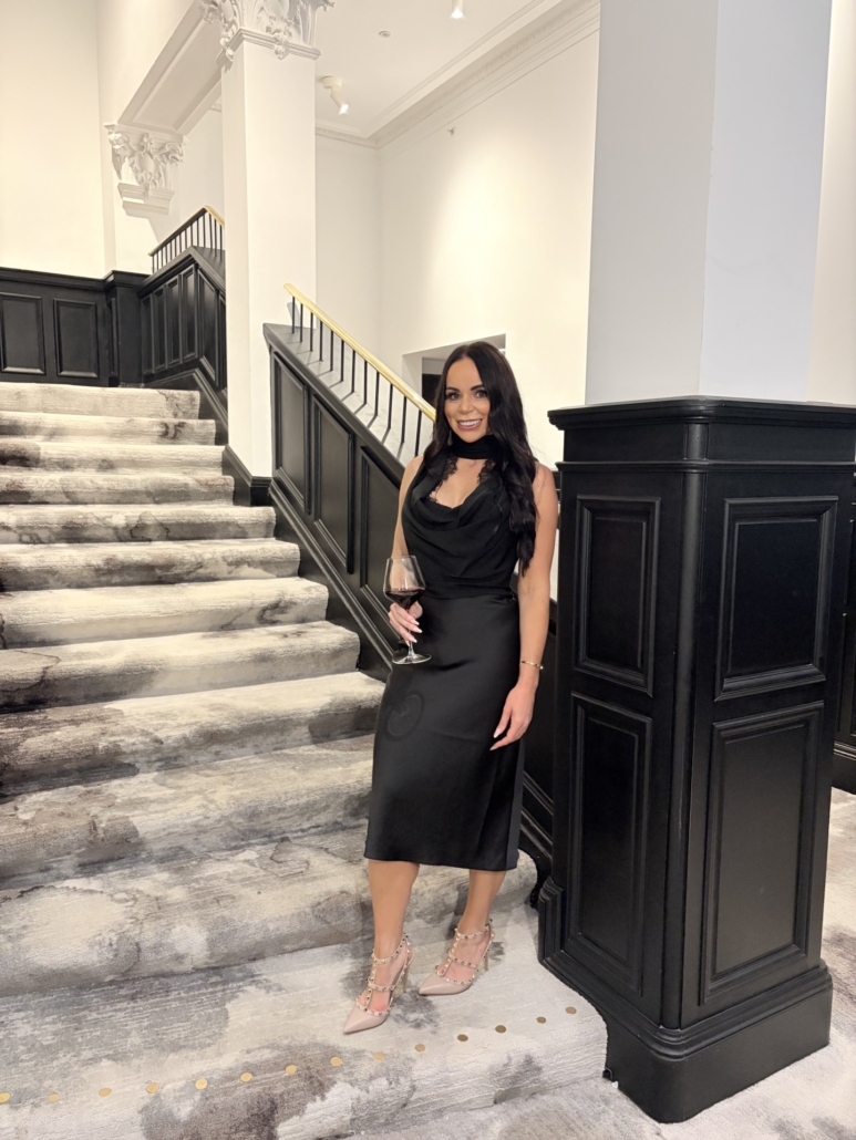 Louize Hollywood in a black dress beside a staircase.